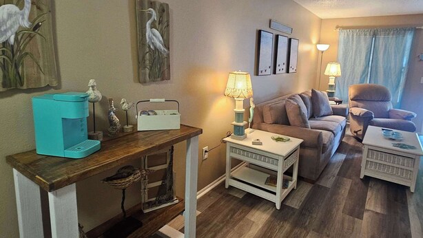 A cozy living room with a wooden coffee table, a sofa, and a small white side table. There are wall-mounted picture frames and a lamp on a side table. - Professor Rousseau's Sea Turtle Sanctuary (Crystal River)