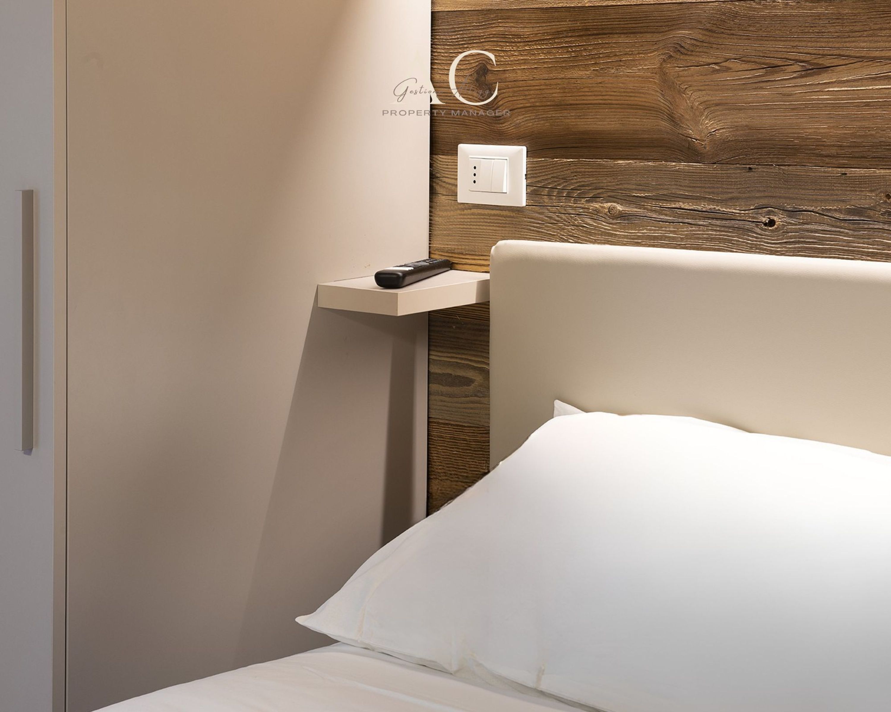 A modern bedroom with a wooden headboard, a bedside table, and a remote control.