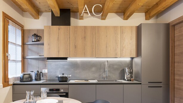 Een moderne keuken met houten kastjes, een roestvrijstalen afzuigkap, een inbouwoven, een spoelbak en een koffiezetapparaat.