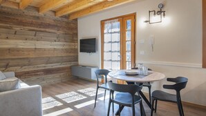 Een gezellige kamer met een houten plafond, een aan de muur bevestigde televisie, een eettafel met stoelen en een raam met uitzicht.