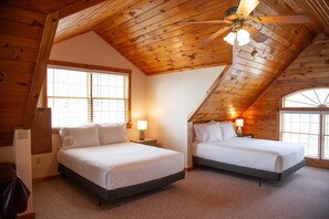 A bedroom with two beds, wooden ceiling beams, and large windows.