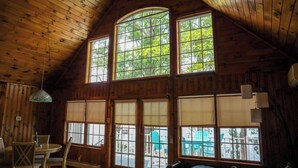 Una cabaña de madera con ventanas amplias, un comedor con sillas y un banco.