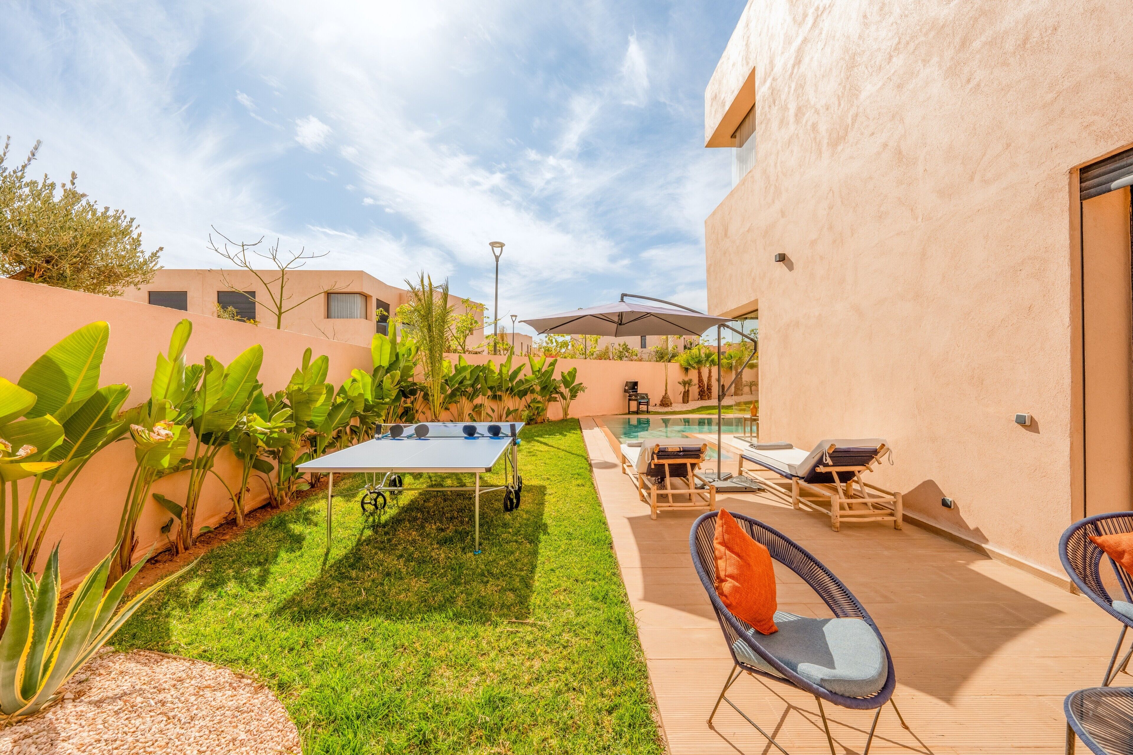 A patio with a pool, lounge chairs, and a ping pong table.