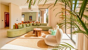 Un salon moderne avec un canapé d’angle vert, un fauteuil blanc et une table basse ronde en bois.