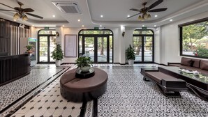 Una hall d'albergo con pavimento decorato, una reception, zone salotto, ventilatori a soffitto e ampie finestre.