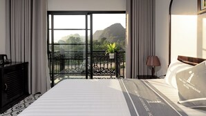 Una camera d'albergo con un letto grande, un comodino, una lampada, una pianta in vaso e un balcone con vista sulle montagne.