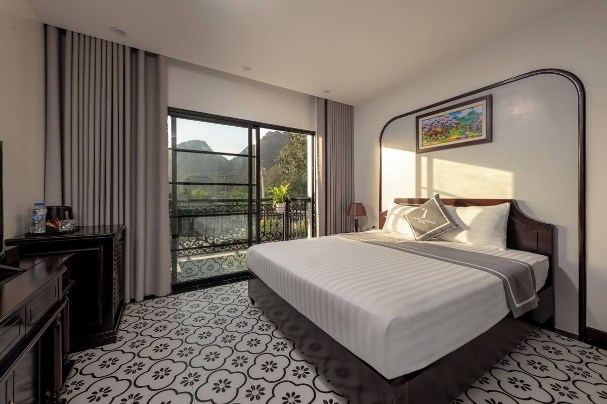 A hotel room with a large bed, a desk with a lamp, and a view of mountains through a window.
