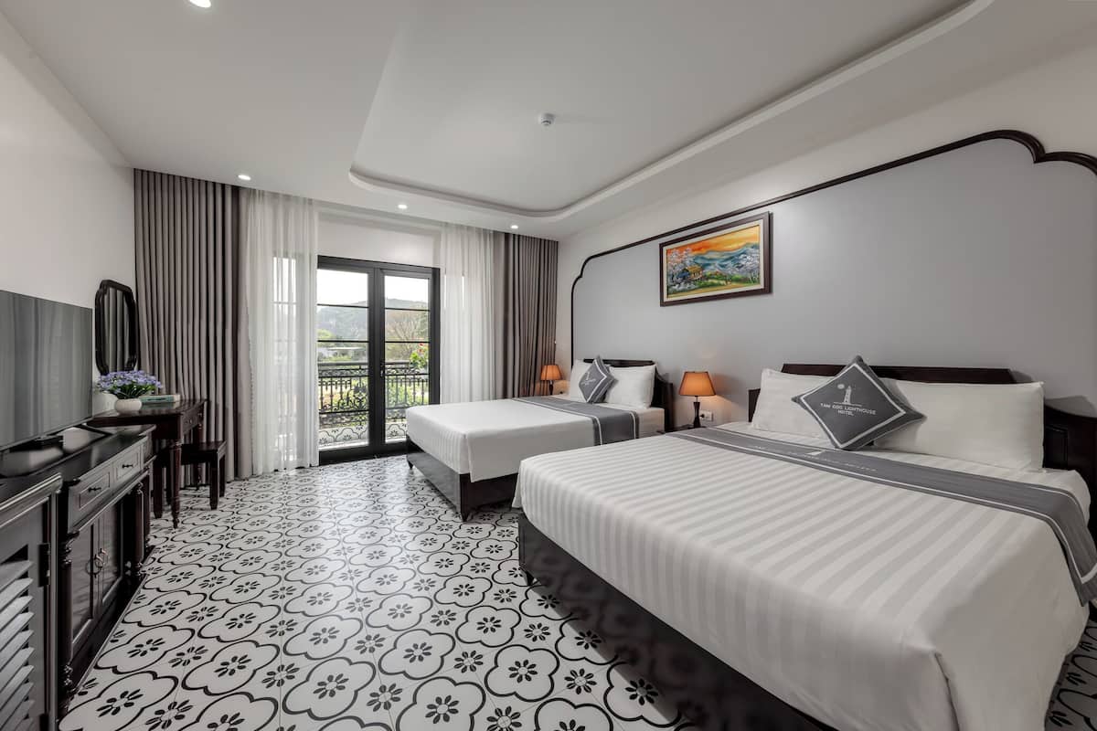 A hotel room with two beds, a desk, a TV, and a balcony with curtains.
