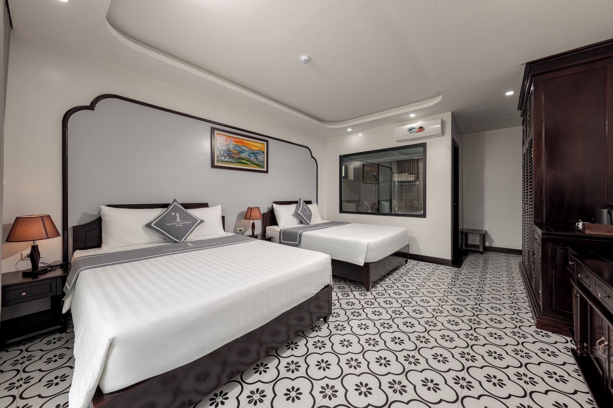 A hotel room with two beds, a large mirror, a painting on the wall, and a patterned floor.