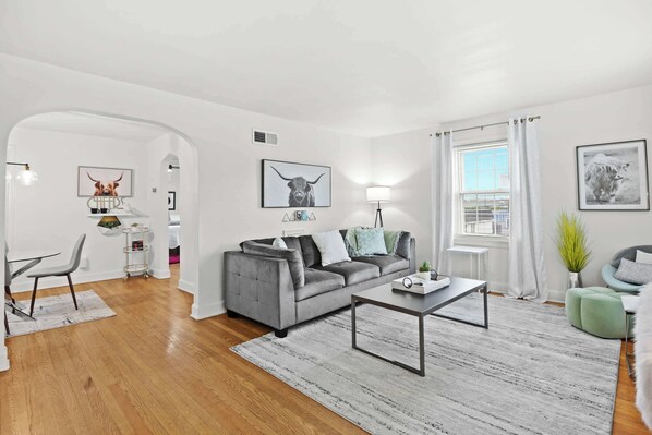 A modern living room with a grey sofa, a coffee table, and a dining area with a chair and table.