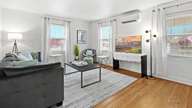 Un salón moderno con un sofá gris, una mesa de centro y vistas de un paisaje urbano a través de grandes ventanales.