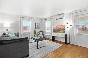 A modern living room with a grey sofa, a coffee table, a floor lamp, and a view of a cityscape through large windows.