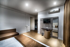 Quarto de hotel moderno com cama, um pequeno espaço para sentar, TV e espelho.