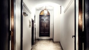 A narrow hallway with a dark wooden door at the end, a white wall, and a textured floor. - Trinità Grand Suite (Rome)
