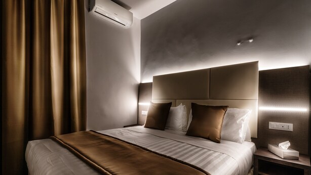 A modern hotel room with a large bed, a bedside table with a lamp, and a wall-mounted air conditioner. - Trinità Grand Suite (Rome)
