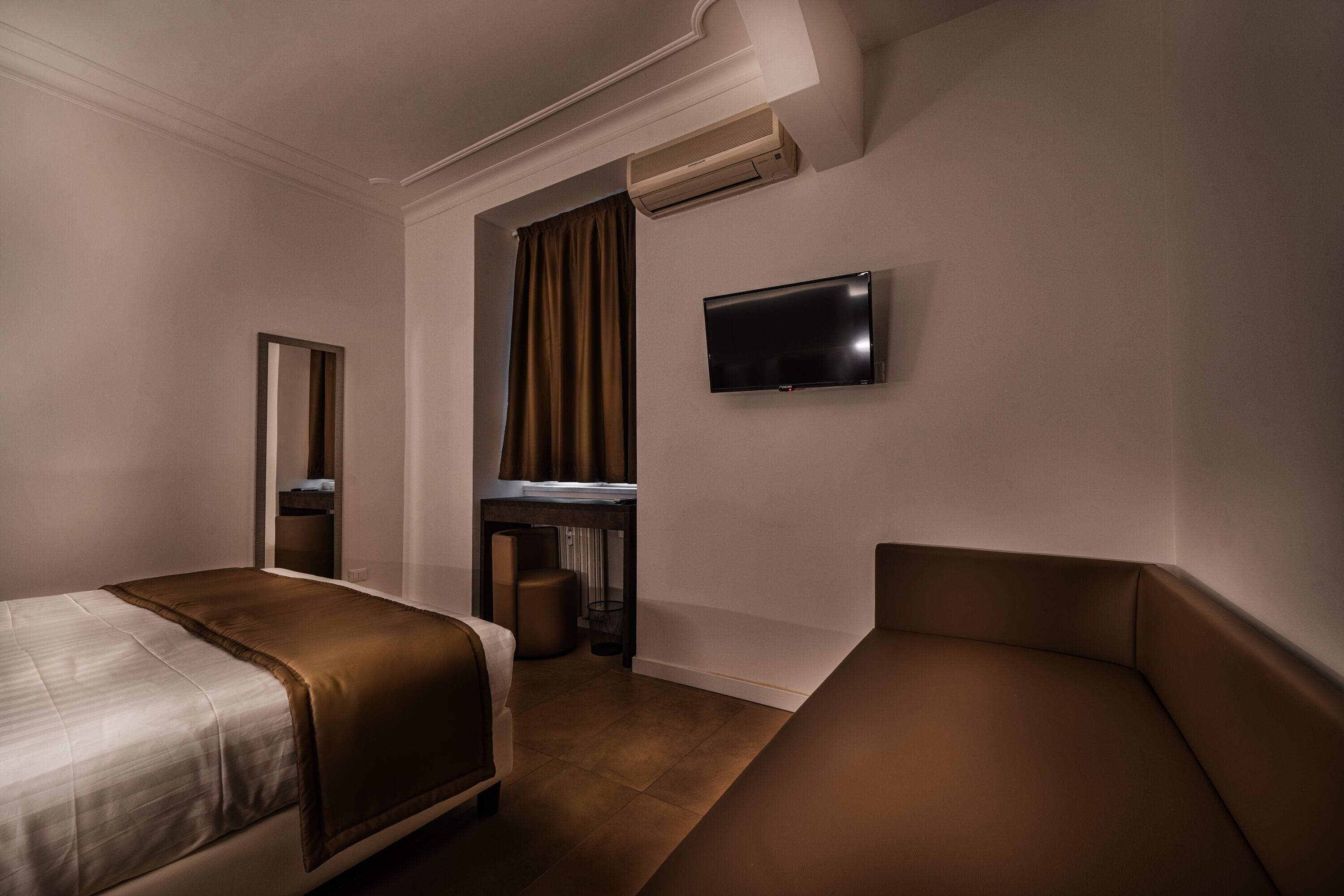 Een hotelkamer met een bed, een bureau, een stoel, een televisie en een airconditioning.