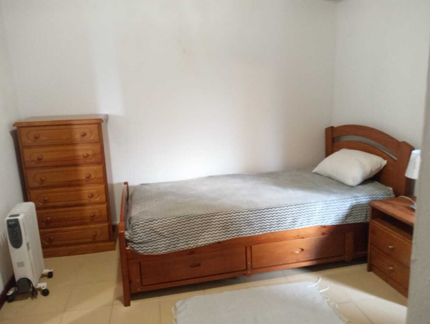 Un dormitorio pequeño y sencillo con una cama y un aparador de madera, además de un radiador.
