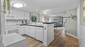 A modern kitchen with white cabinets, a central island, and a dining area with a sofa and coffee table.