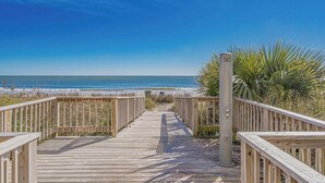 A wooden boardwalk leading to a beach with a clear view of the ocean.
