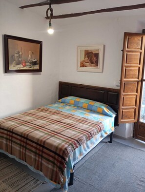 Een slaapkamer met een bed, twee ingelijste schilderijen, een houten deur en een plafondlamp.