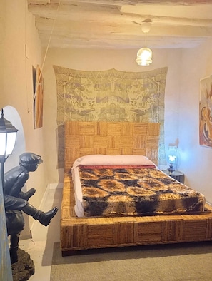 A bedroom with a wooden headboard, a patterned tapestry, a red bedspread, and a statue of a man.