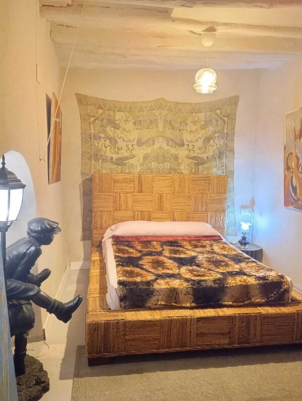 Ein Schlafzimmer mit einem Holzkopfteil, einer gemusterten Wandteppich, einer roten Bettdecke und einer Statue eines Mannes.