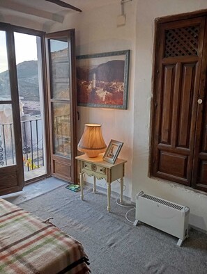 Een kamer met een bed, een tafel met een lamp, een lijst met een afbeelding en een radiator.