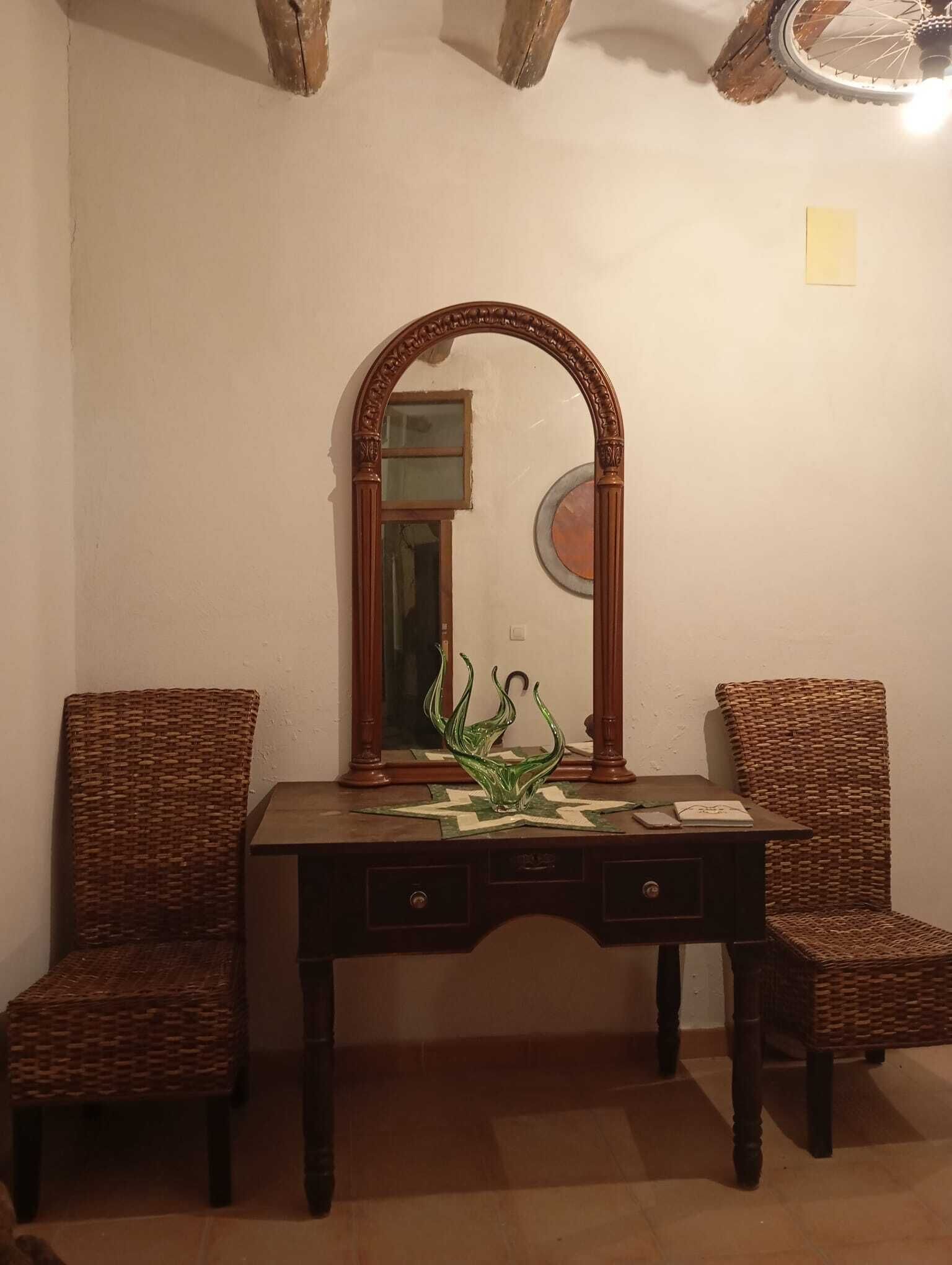 Une pièce comprenant un bureau en bois, deux fauteuils en osier, un miroir et un vase décoratif en verre.