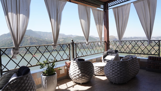 Un balcon donnant sur un lac et des montagnes, aménagé avec des chaises rondes en osier et une plante en pot.