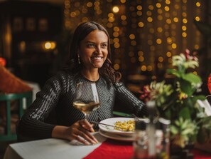 Une personne assise à une table, devant un verre de vin, une assiette de nourriture et un vase rempli de fleurs.