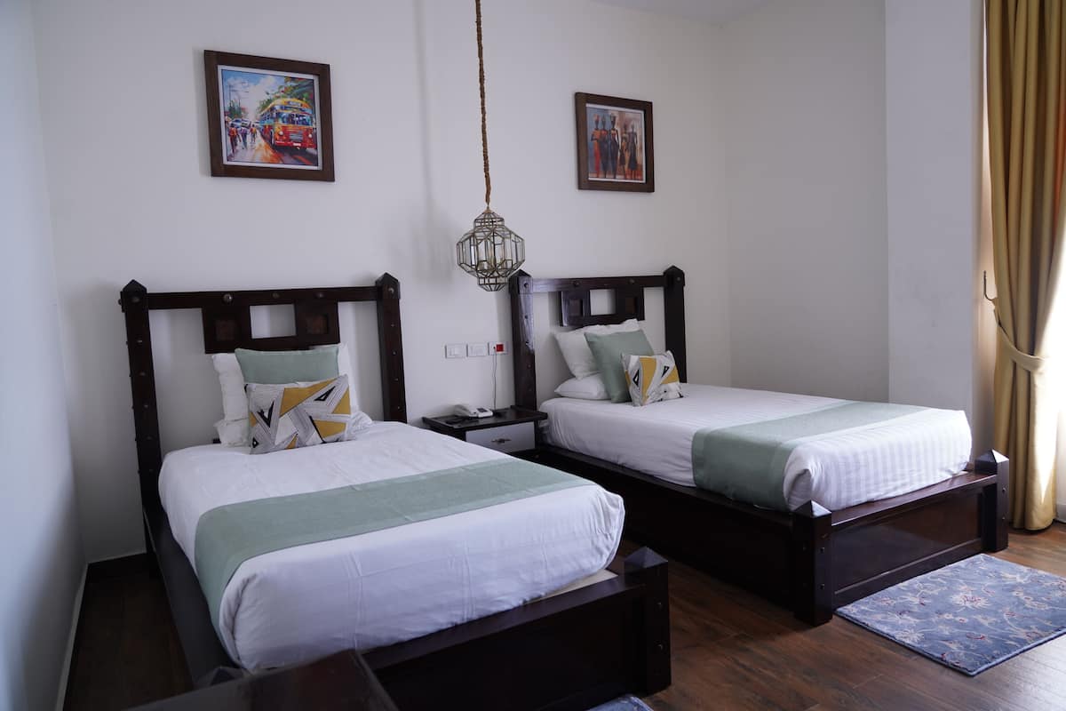 Dos camas individuales con estructura de madera, ropa de cama blanca y almohadones decorativos.
