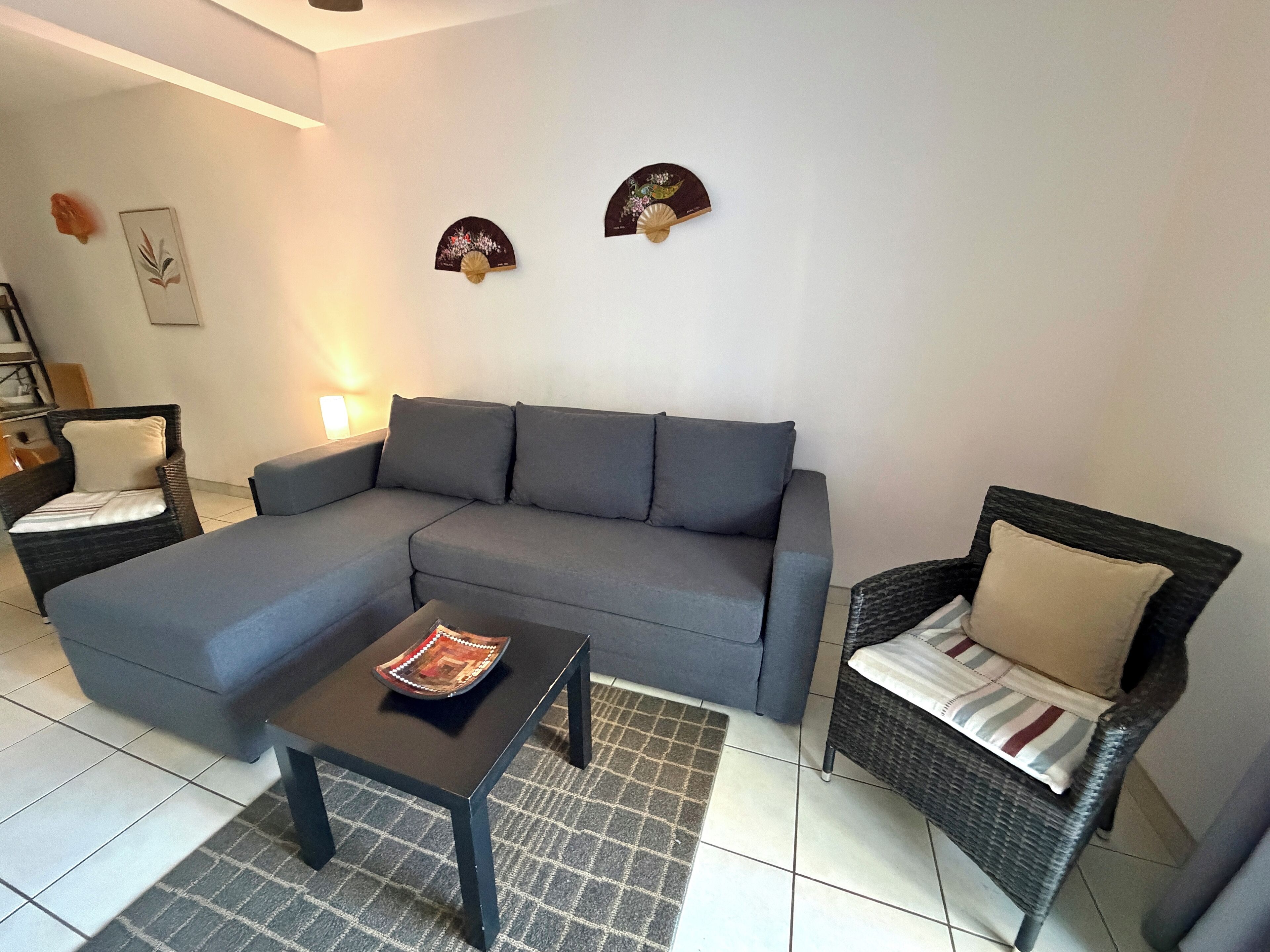 A living room with a grey sectional sofa, two wicker chairs, a small black table, and decorative wall art.