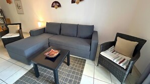 Una sala de estar con un sofá seccional gris, dos sillas de mimbre, una mesita negra y decoración en la pared.