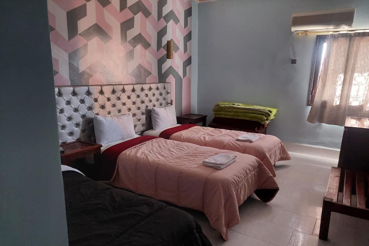 A room with two beds, a patterned wall, and a window with curtains.