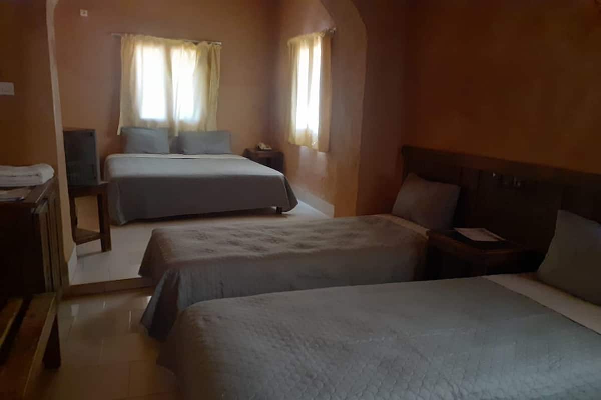 A hotel room with two beds, a bedside table, a nightstand, and a window with curtains.
