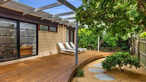Una terrazza esterna moderna con poltrone relax, pavimento in legno e un’area giardino con lastre di pietra.