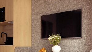 Ein modernes Wohnzimmer mit einem an der Wand befestigten Flachbildfernseher, einem runden Tisch mit Blumenvase und zwei grau gepolsterten Sesseln.
