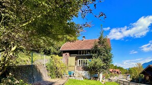 Ein Haus mit einem geneigten Dach, umgeben von einem gepflegten Garten und einer Steinmauer.