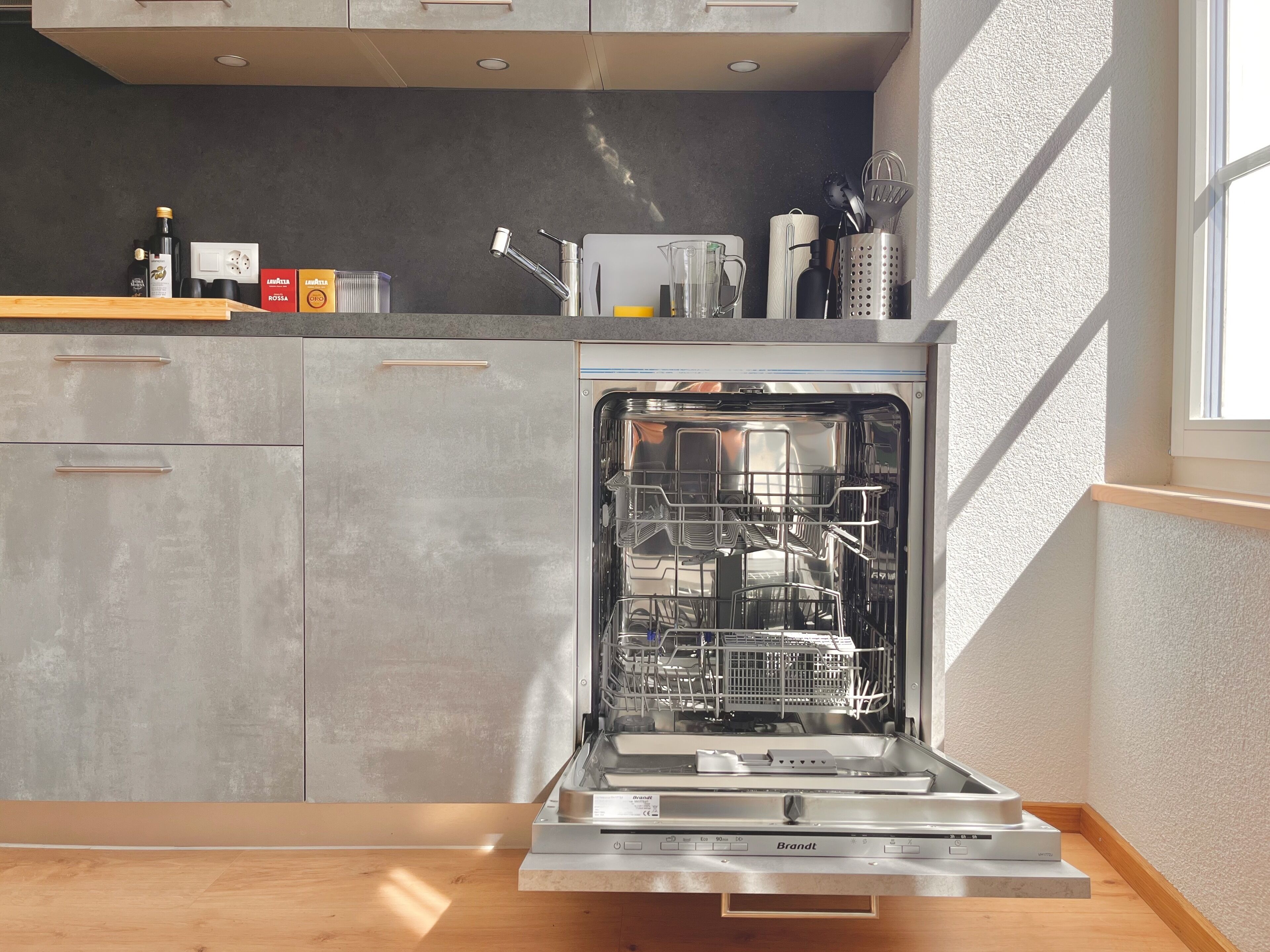 Une cuisine moderne dotée d’un lave-vaisselle encastré, de meubles gris et d’un plan de travail en bois.
