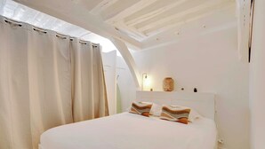 A bedroom with a large bed, white walls, and a sloped ceiling. - Elegant Apartment -2br-4p- Le Marais (Paris)