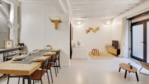 A modern dining area with a wooden table set for four, a white sofa, and a TV on a wooden stand. - Elegant Apartment -2br-4p- Le Marais (Paris)