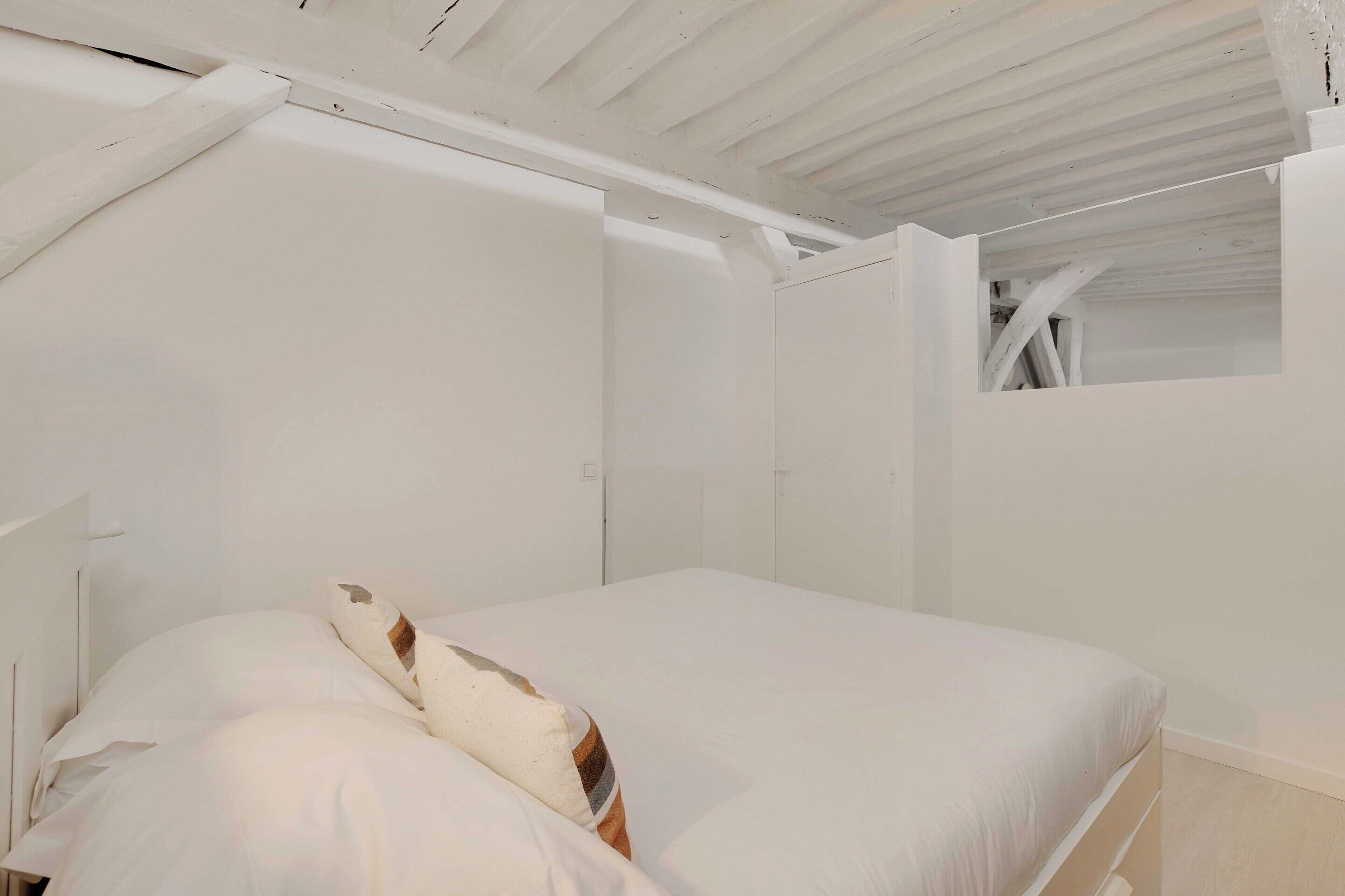Een witte kamer met een bed, een raam en een schuine plafond.