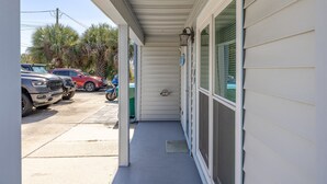 A covered porch with a concrete floor, a green trash bin, and a blue doorbell. - Seas the Day, Pet Friendly - Walk to public beach! (Panama City Beach)