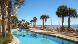 A pool area with lounge chairs and palm trees, overlooking a beach.