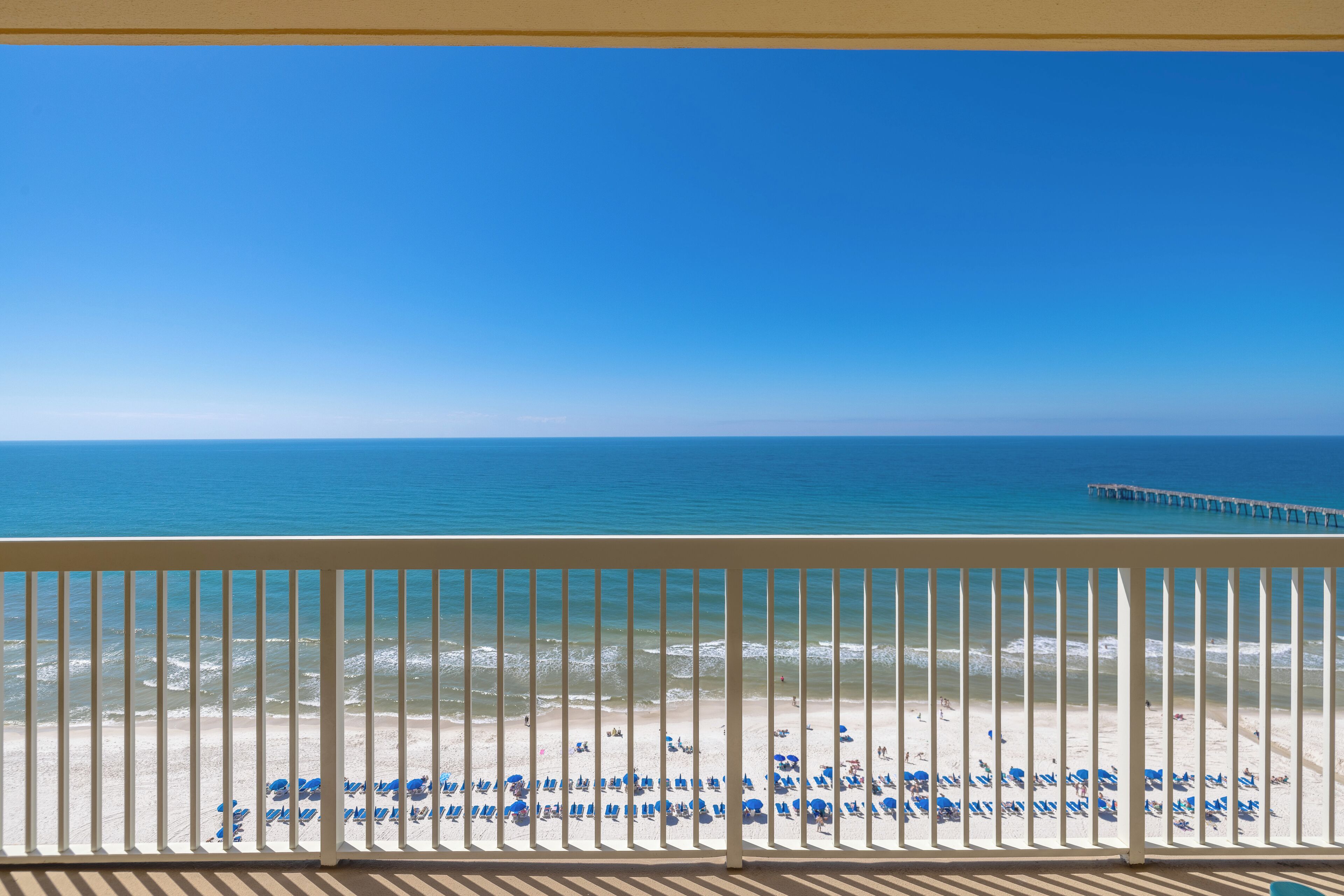 A balcony with a view of a beach, a pier, and a clear blue sky.