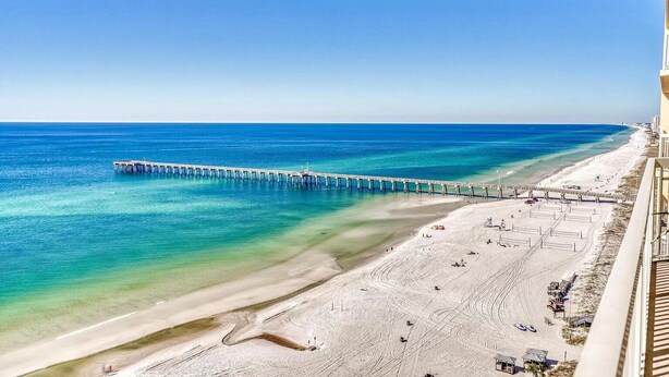 A beach with a pier extending into the ocean, sandy beach, and a clear sky.