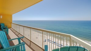 A balcony with turquoise chairs overlooking a beach with umbrellas.