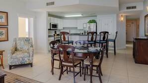 A spacious living area with a dining table and chairs, a comfortable armchair, and a kitchen with white cabinets and appliances.