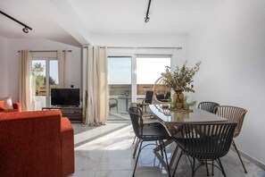 Una sala moderna con sofá, televisión, mesa de comedor, sillas y un balcón con vistas.
