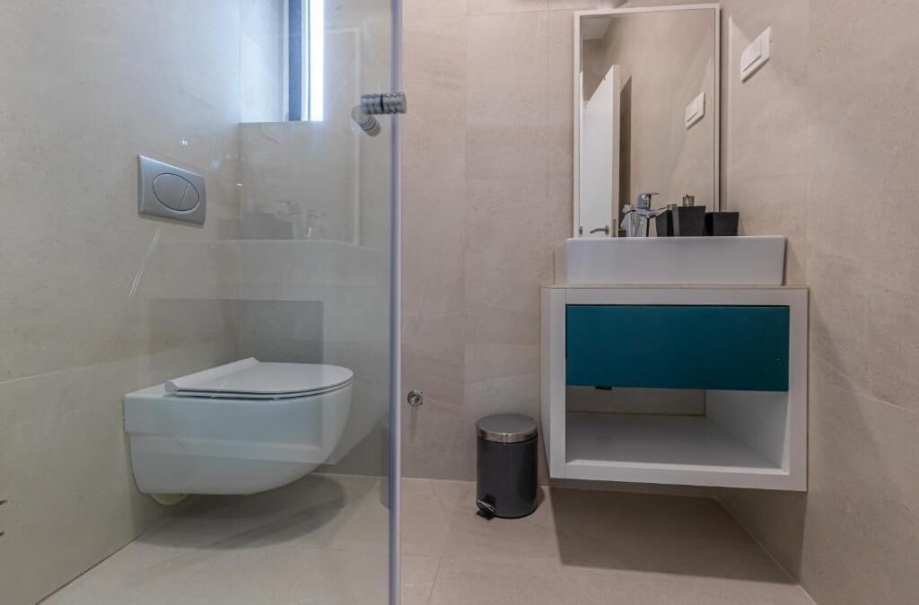 A modern bathroom with a glass-enclosed shower, a white toilet, a sink with a blue cabinet, and a mirror above the sink.